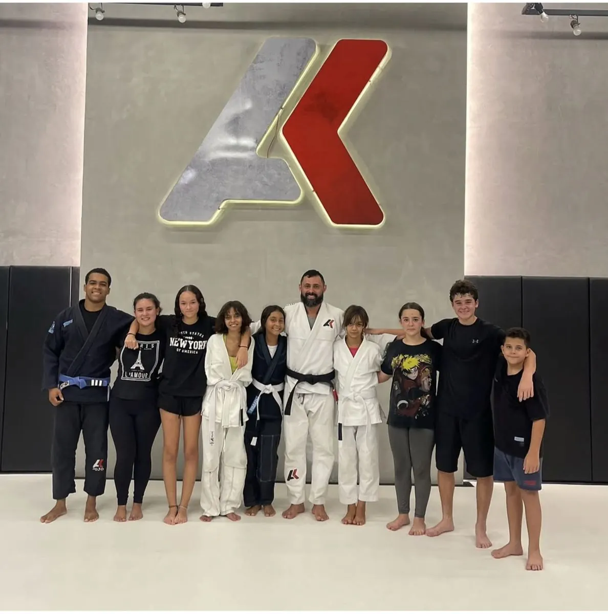 Professor e alunos do instituto posam juntos diante do logotipo da academia