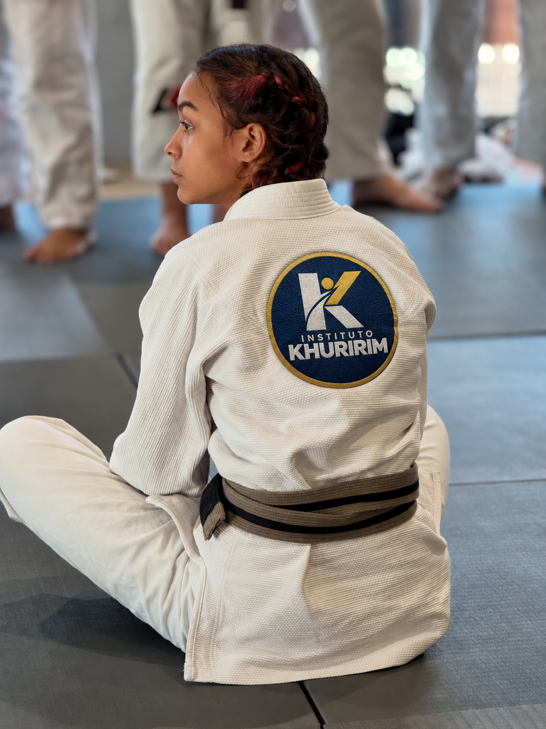 Jovem de kimono sentada no dojo com o emblema do Instituto Khuririm nas costas